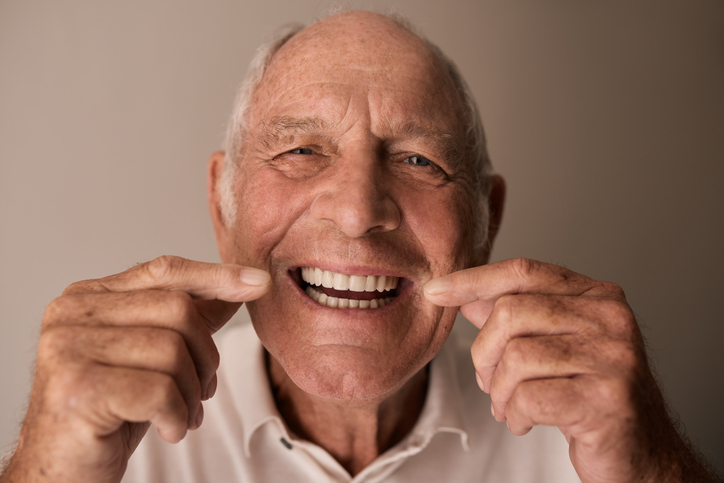 Ecstatic senior man pointing at his new smile with dental implants.