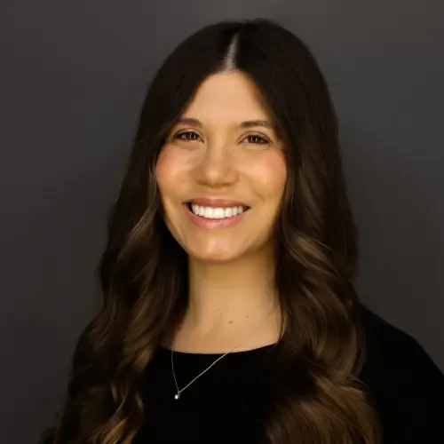 Portrait of a smiling woman with long wavy brown hair, wearing a black top and a silver necklace.