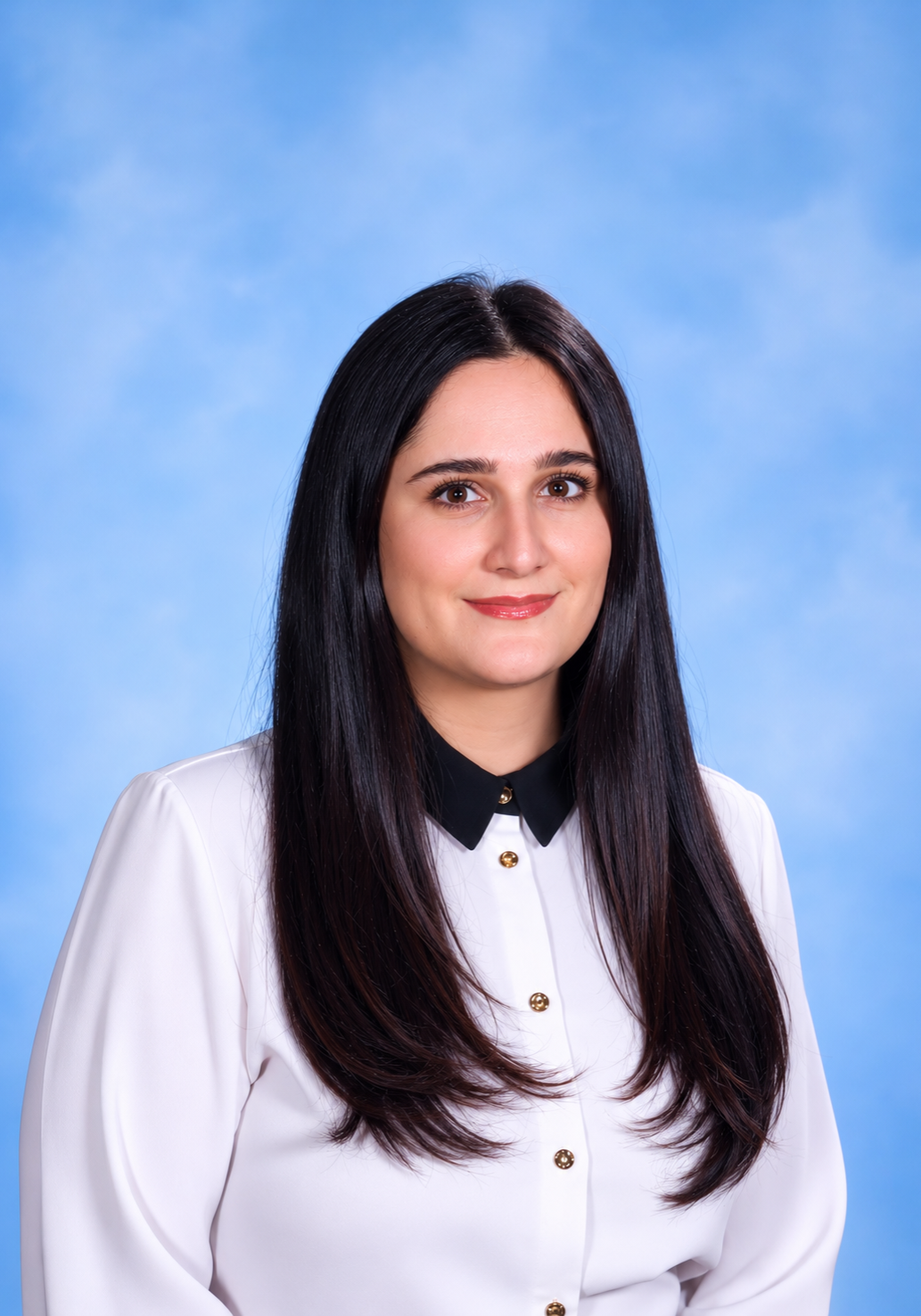 Professional headshot of a smiling woman with long dark hair, wearing a white blouse with a black collar, against a blue backdrop.